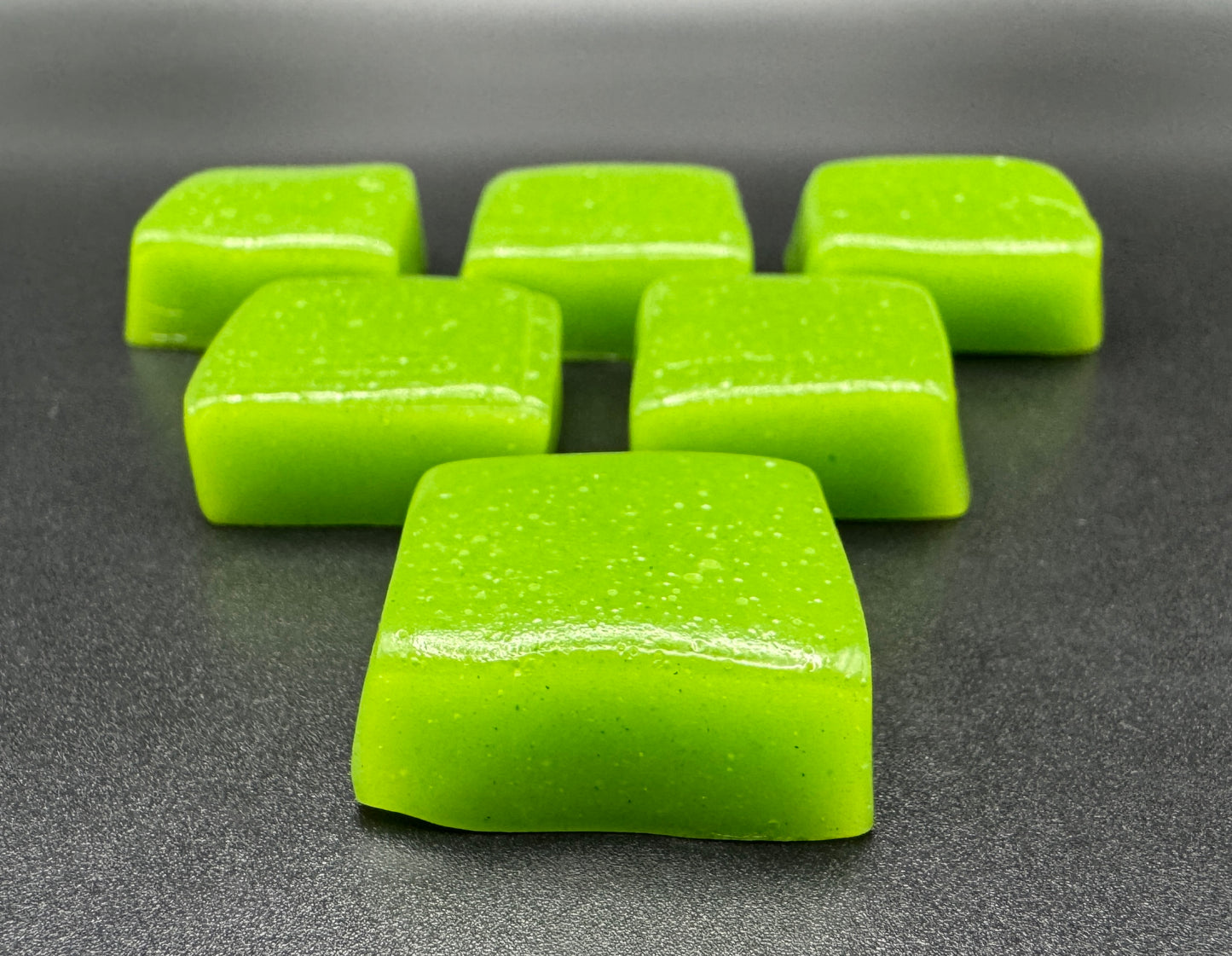 A group of green, chewy candy pieces arranged on a dark surface.