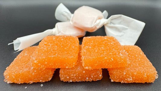 Orange Gummy candy with sweet and sour sugar on top. Two wrapped candies in the background.