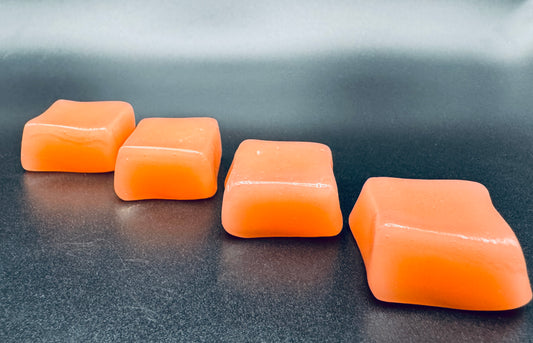 Four orange square-shaped watermelon chews on a dark background.